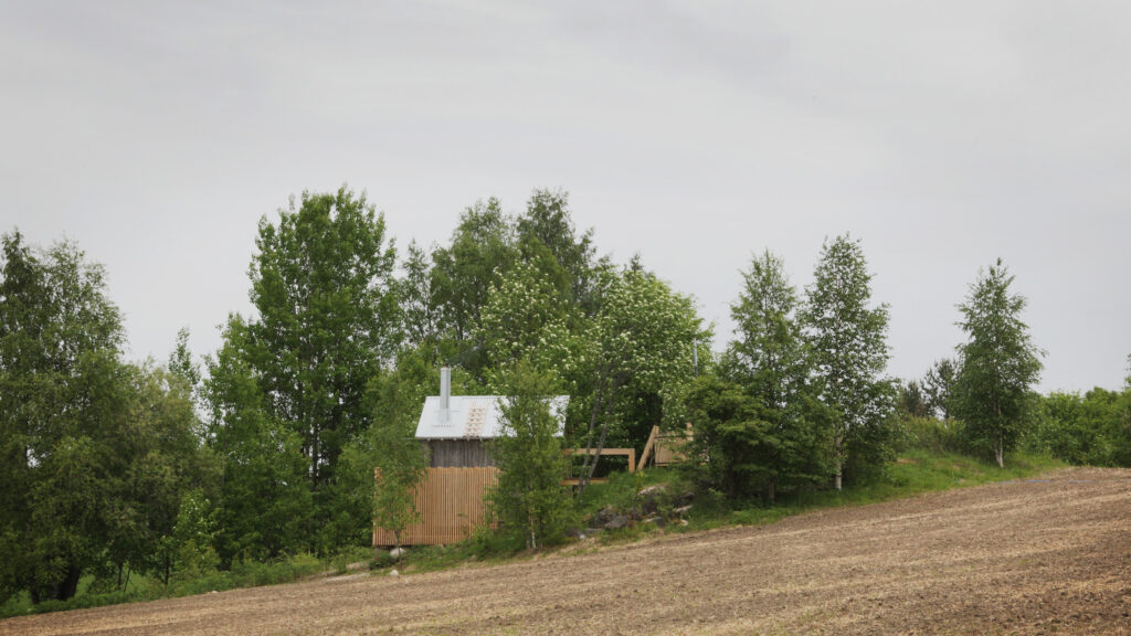 A small sauna building in a landscape with a hill and forest