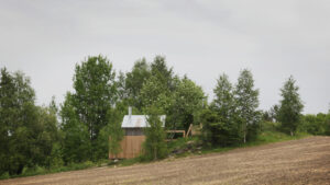A small sauna building in a landscape with a hill and forest