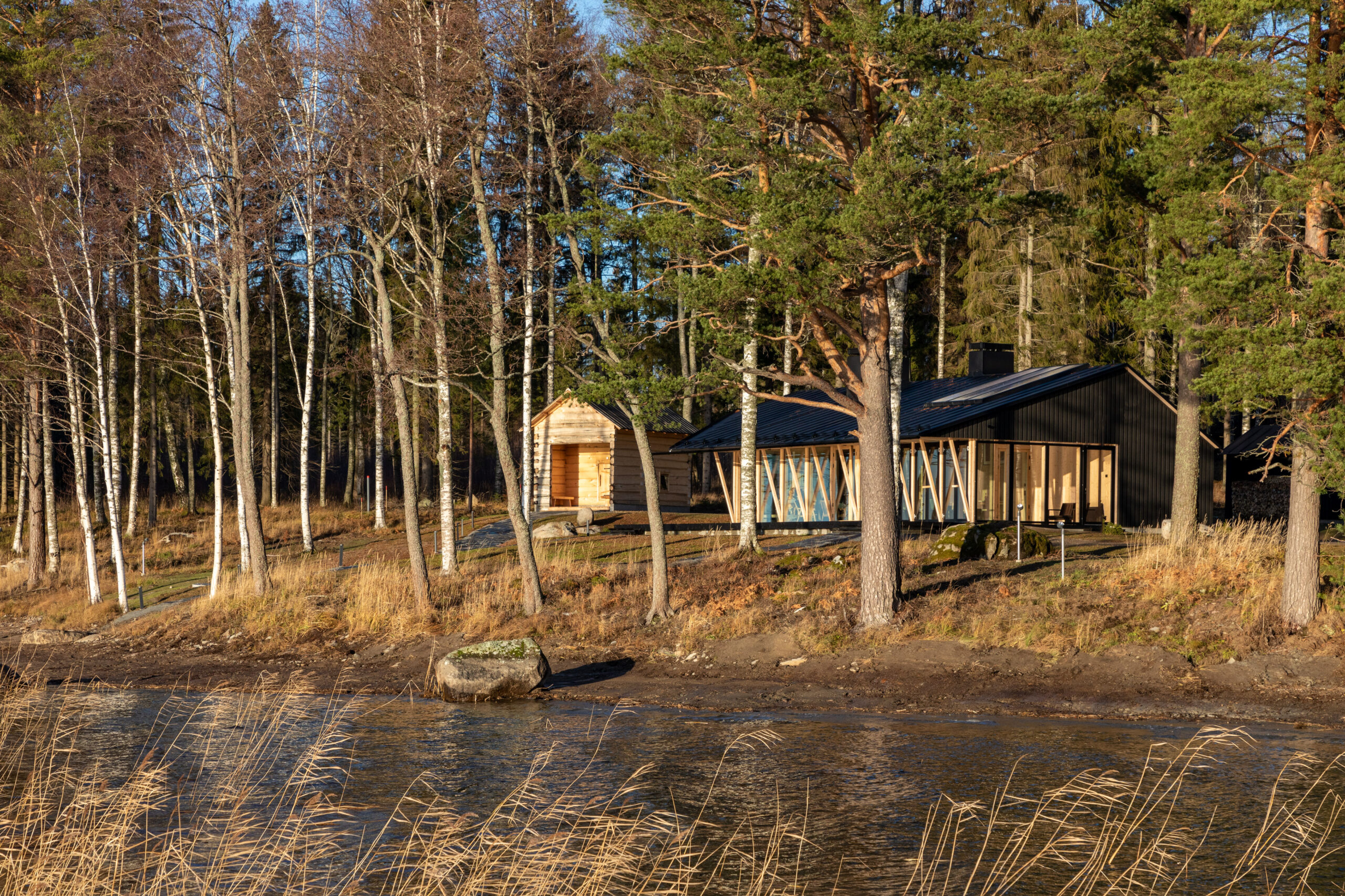 The two new sauna buildings by the lake, one is a smoke saune made of hand carved logs, the other is a larger sauna with a fireplace room and a terrace made of CLT