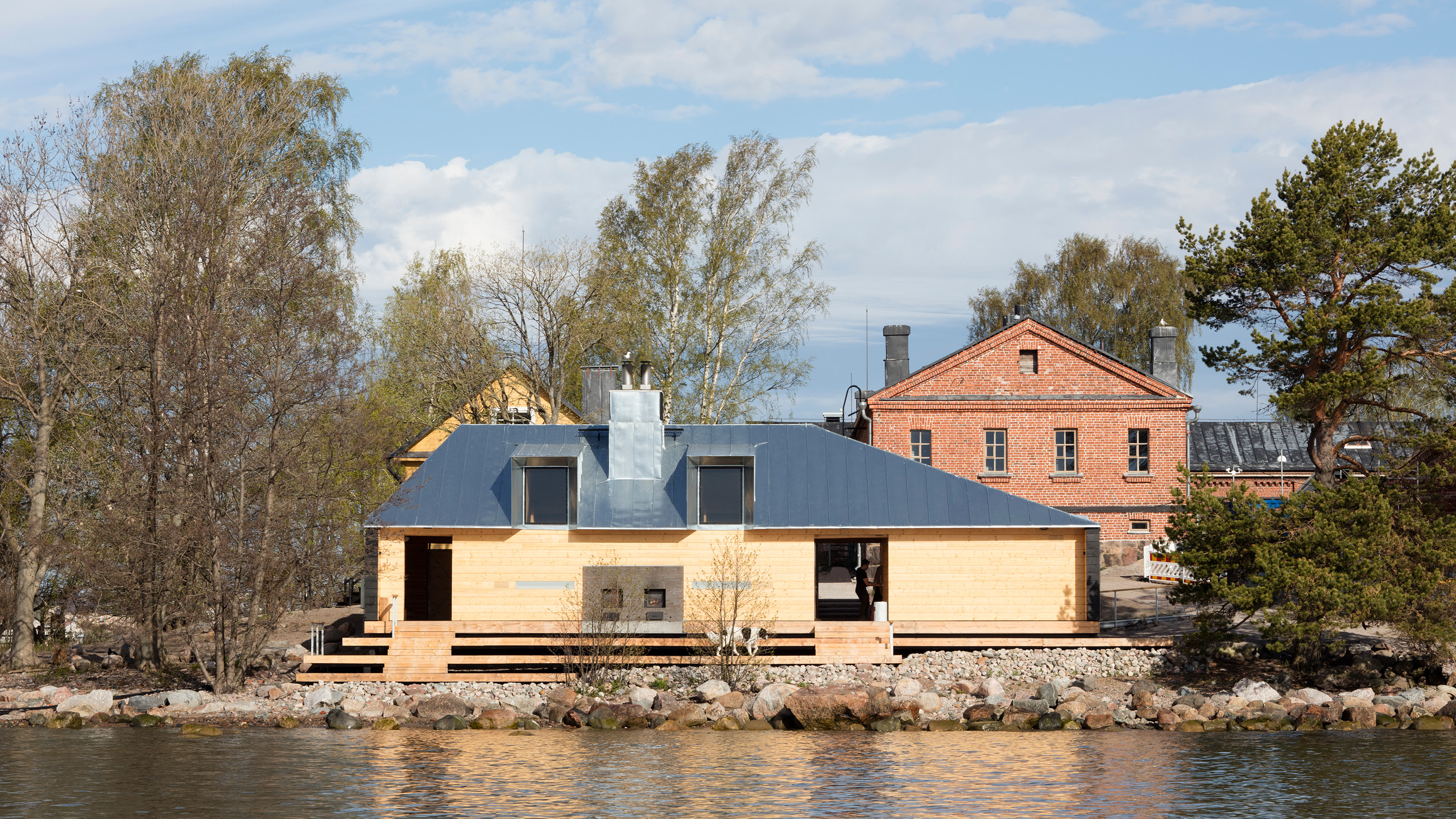 A wooden sauna by the sea with a dog standing on the terrace