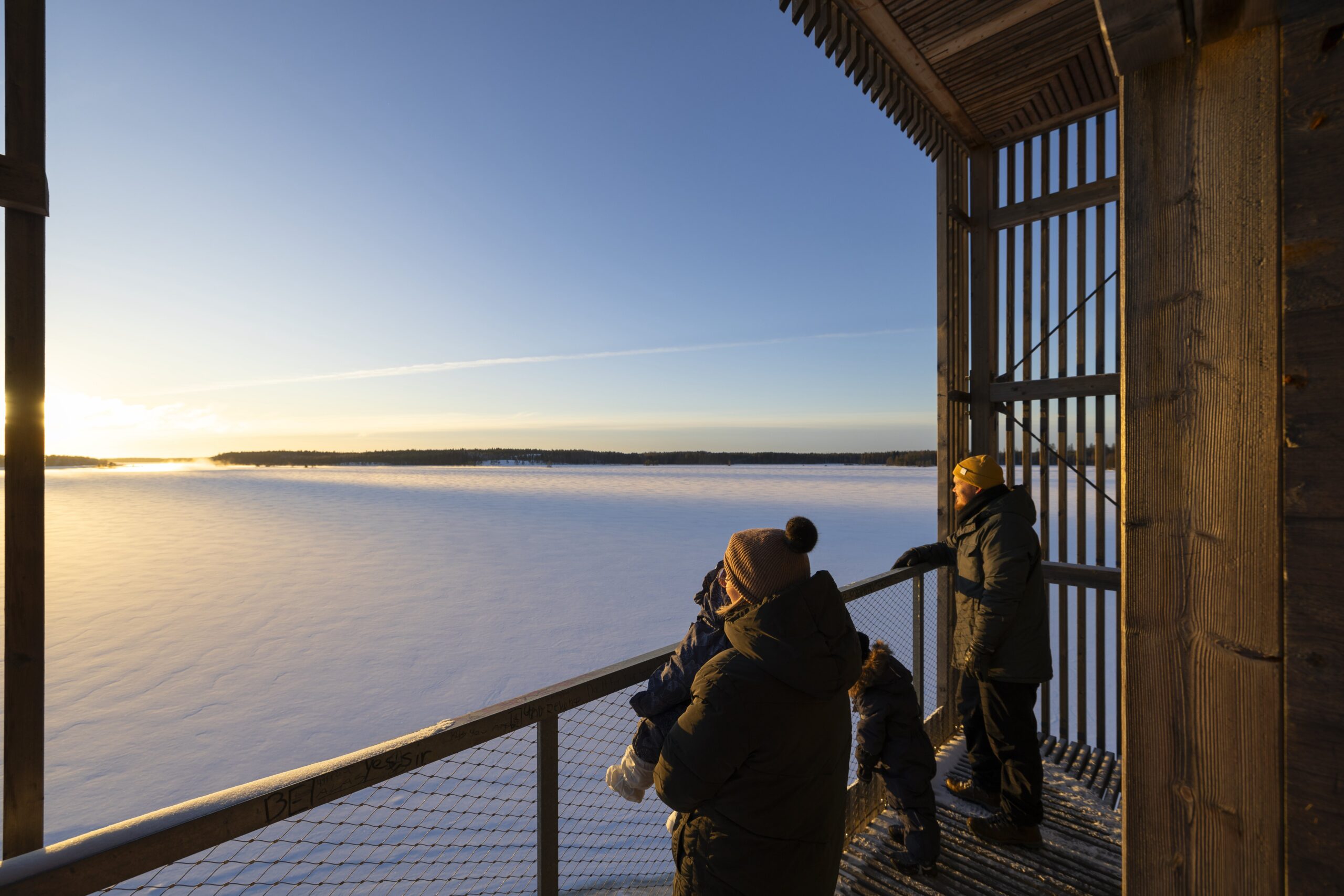 People on a wooden observation deck viewing the sunset over the lake in the winter