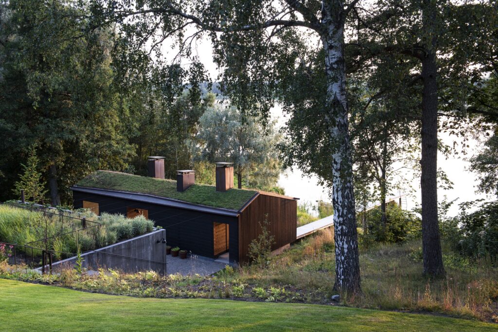 Wooden sauna with a green roof seen from the hill looking down to the lake