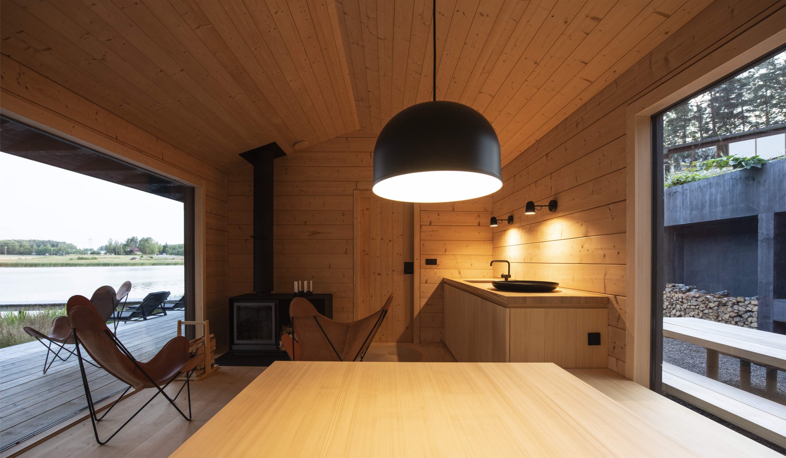 View of the fireplace room with large windows opening to the lake on one side and to the garden with an outdoor kitchen on the other side